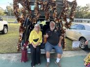 A man and woman sitting on the open hatch of a van under a gold glittery wreath