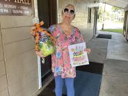 A woman holding a colored page and a basket of gifts outside of Town Hall.