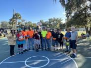 A group of people dressed for Halloween holding baskets of candy on an outdoor basketball court