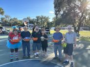 A group of people dressed for Halloween holding baskets of candy on an outdoor basketball court